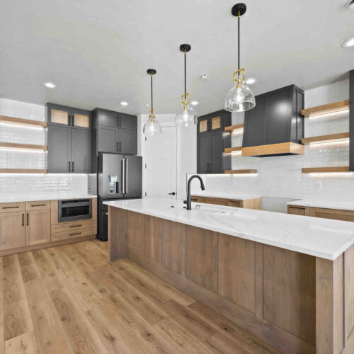 angled view of the kitchen featuring the large kitchen island, accent overhead lighting, shelves, cabinetry and black slate appliances
